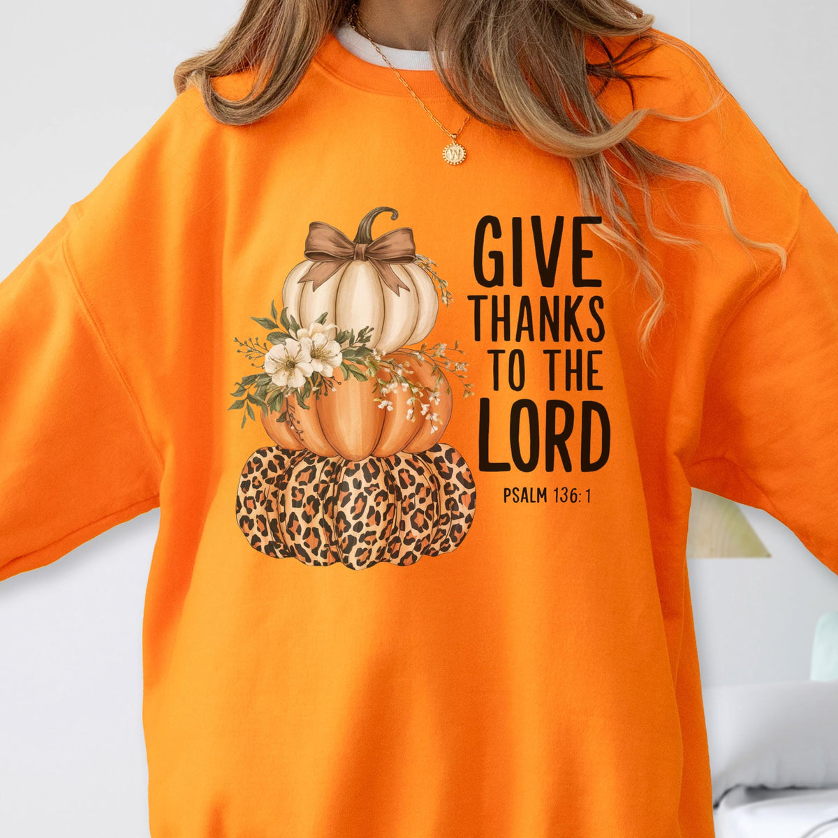 May include: Orange sweatshirt featuring a stacked pumpkin design with a leopard print base, a middle pumpkin, and a top pumpkin with a bow. The text "GIVE THANKS TO THE LORD" is printed in black, with "PSALM 136:1" below.