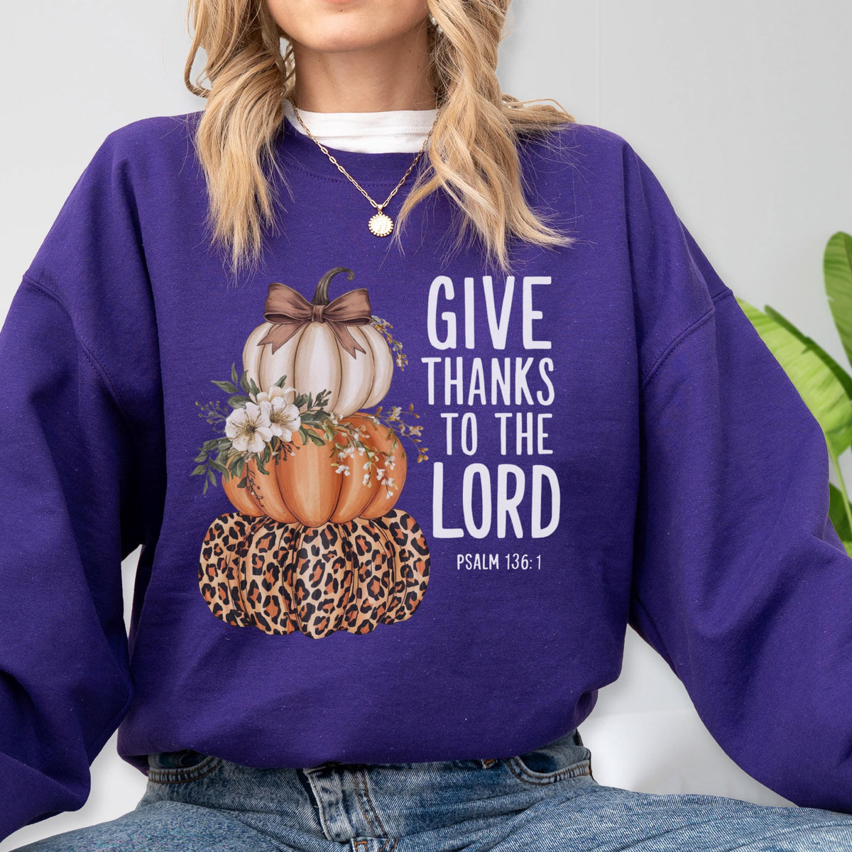 May include: A purple sweatshirt featuring a stacked pumpkin design with a leopard print base, orange and white pumpkins, and the text "GIVE THANKS TO THE LORD" in white. Psalm 136:1 is printed below the text.