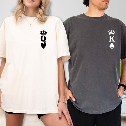May include: A cream-colored t-shirt featuring a black graphic of a crown above the letter Q and a heart symbol, and a charcoal gray t-shirt featuring a white graphic of a crown above the letter K and a spade symbol on the chest area.