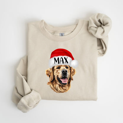 May include: A beige sweatshirt featuring a graphic of a Golden Retriever wearing a red Santa hat with the name "MAX" in white. The sweatshirt has long sleeves and a crew neck. The image is centered on the front of the garment.