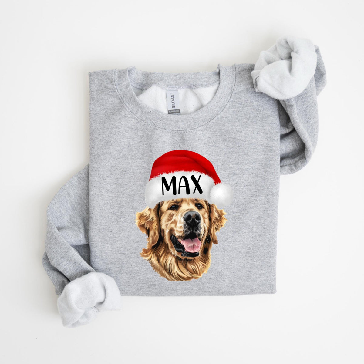 May include: A light gray sweatshirt featuring a golden retriever wearing a red Santa hat with the name "MAX" printed on it. The dog's face is the focal point, with its tongue slightly visible. The sweatshirt's sleeves are rolled up.