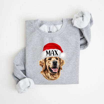 May include: A light gray sweatshirt featuring a golden retriever wearing a red Santa hat with the name "MAX" printed on it. The dog's face is the focal point, with its tongue slightly visible. The sweatshirt's sleeves are rolled up.