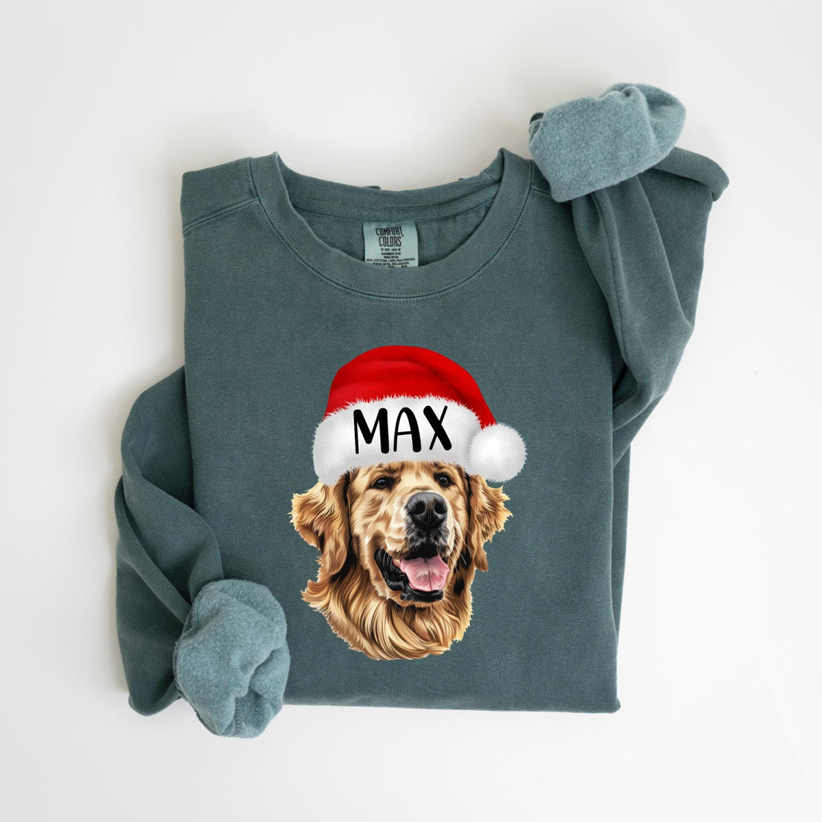 May include: A teal-colored sweatshirt featuring a golden retriever wearing a red Santa hat with the name "MAX" printed on it. The dog's face is detailed with a happy expression. The sweatshirt has cuffed sleeves.