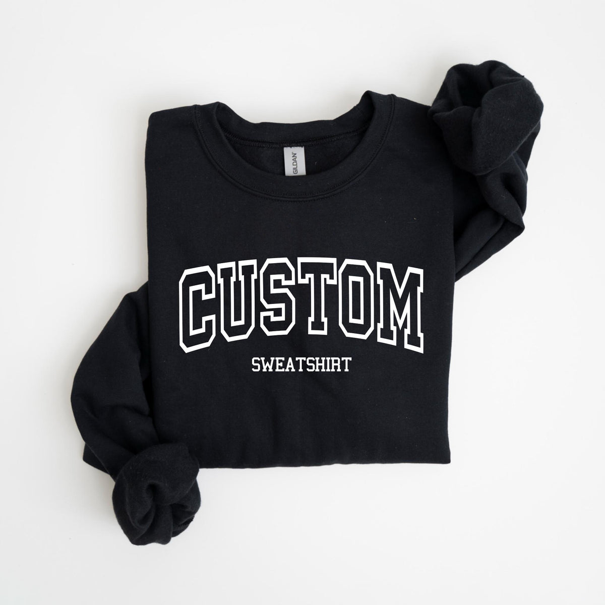 May include: Black sweatshirt with the word "CUSTOM" in white, outlined block letters. Below the word "CUSTOM" is the word "SWEATSHIRT" in a smaller font. The sweatshirt is folded neatly on a white surface.