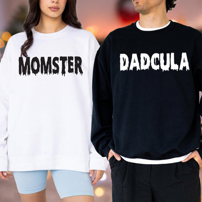 May include: A white sweatshirt with the word "MOMSTER" in black dripping font and a black sweatshirt with the word "DADCULA" in white dripping font. The sweatshirts are worn by two people.