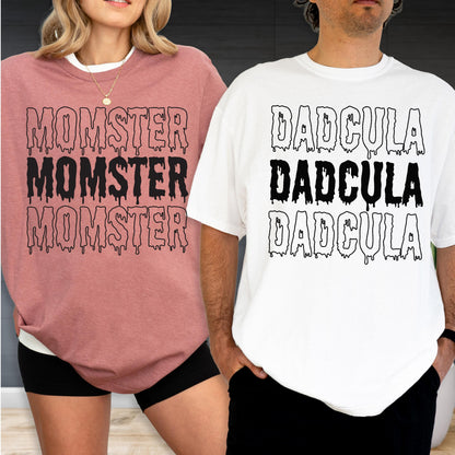 May include: Two t-shirts, one dusty rose and one white, each with a unique graphic. The dusty rose shirt displays the word "MOMSTER" three times in a dripping font. The white shirt features the word "DADCULA" three times in a similar style.