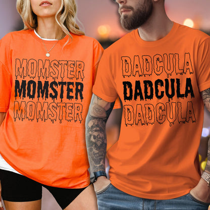 May include: Two orange t-shirts with black text. One shirt says "MOMSTER" three times, and the other says "DADcula" three times. The shirts are short-sleeved and appear to be made of a soft material.