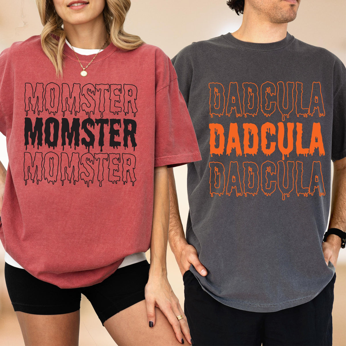 May include: Two short-sleeved t-shirts. One is a reddish-pink color with the word "MOMSTER" in black dripping font. The other is a dark gray color with the word "DADcula" in orange dripping font. Both shirts are oversized.