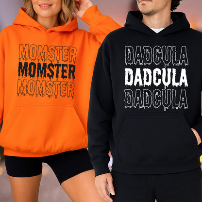 May include: Two hooded sweatshirts, one orange and one black. The orange sweatshirt has the text "MOMSTER MOMSTER MOMSTER" in black dripping font. The black sweatshirt has the text "DADGULA DADGULA DADGULA" in white dripping font.
