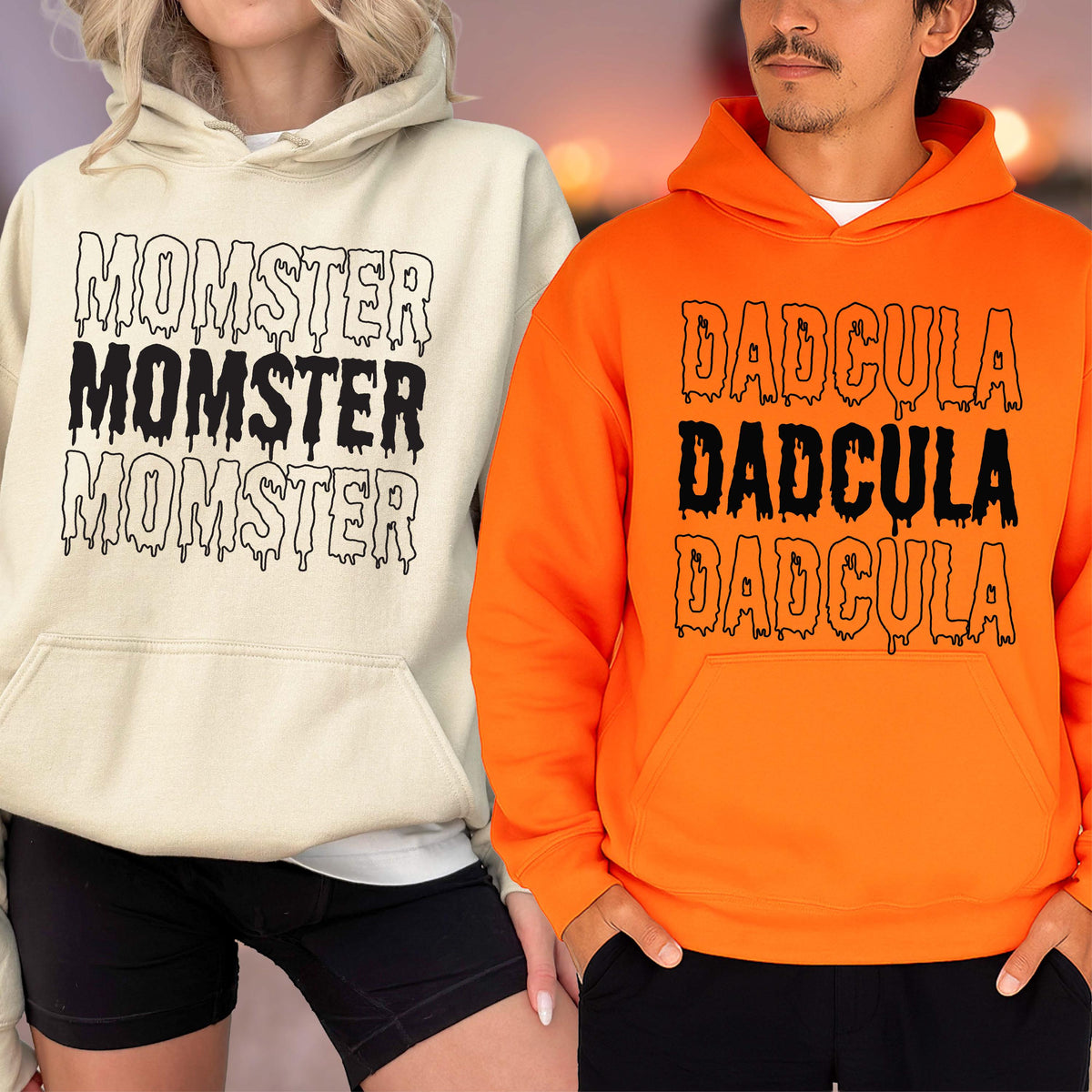 May include: Two hooded sweatshirts, one cream-colored and one orange. The cream-colored sweatshirt has the word "MOMSTER" printed three times in black, dripping font. The orange sweatshirt has the word "DADcula" printed three times in black, dripping font.