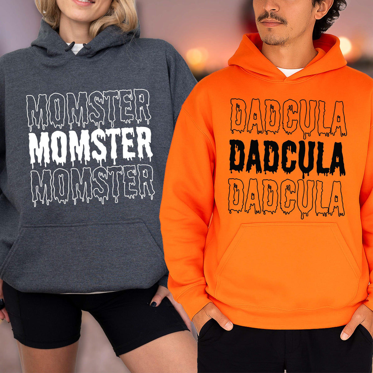 May include: Two hooded sweatshirts, one dark gray and one orange. The dark gray sweatshirt has the word "MOMSTER" printed three times in white, with a dripping effect. The orange sweatshirt has the word "DADCULA" printed three times in black, with a dripping effect.