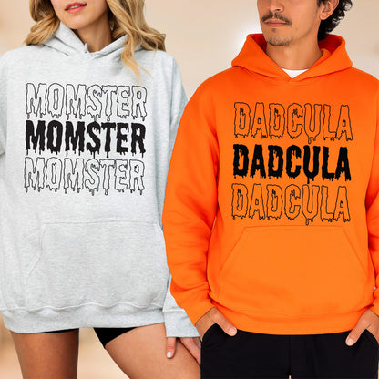 May include: Two hooded sweatshirts, one light gray and one orange. The gray sweatshirt has the word "MOMSTER" printed three times in black, dripping font. The orange sweatshirt has the word "DADcula" printed three times in black, dripping font.