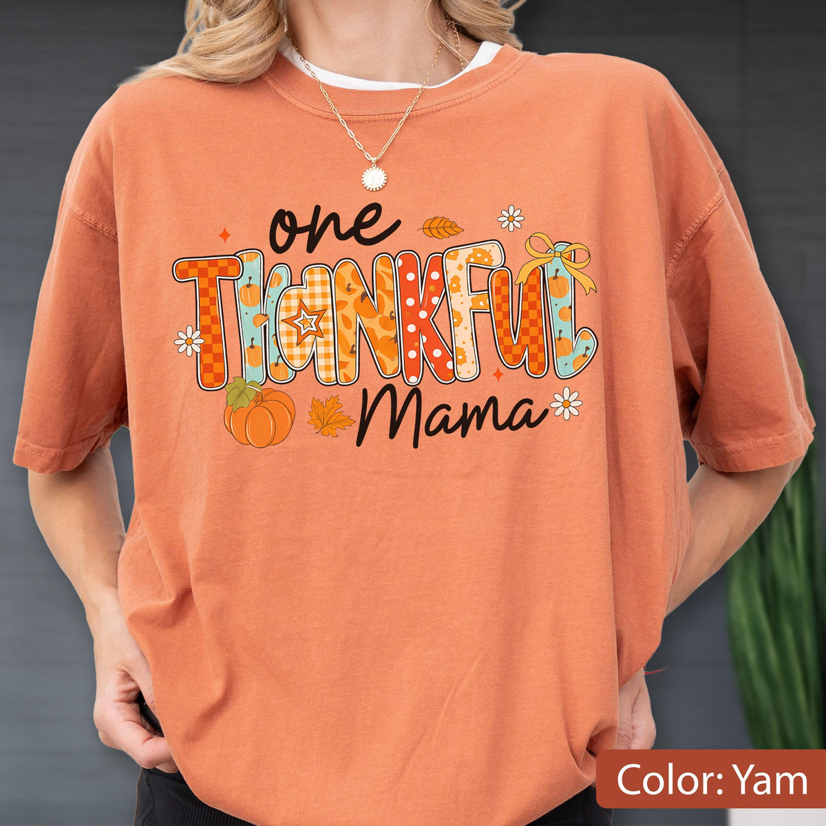 May include: Orange t-shirt with the text "one THANKFUL Mama" in a colorful, fall-themed design. The design includes pumpkins, leaves, and floral accents. The shirt is a solid orange color.