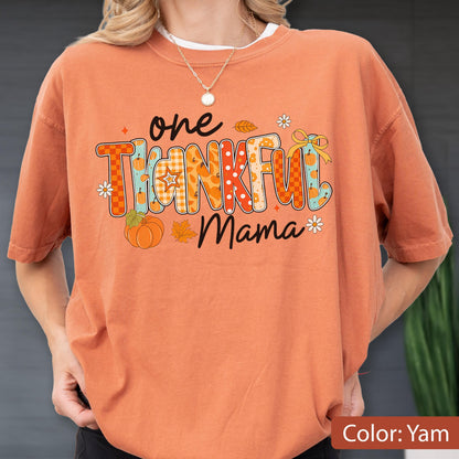 May include: Orange t-shirt with the text "one THANKFUL Mama" in a colorful, fall-themed design. The design includes pumpkins, leaves, and floral accents. The shirt is a solid orange color.