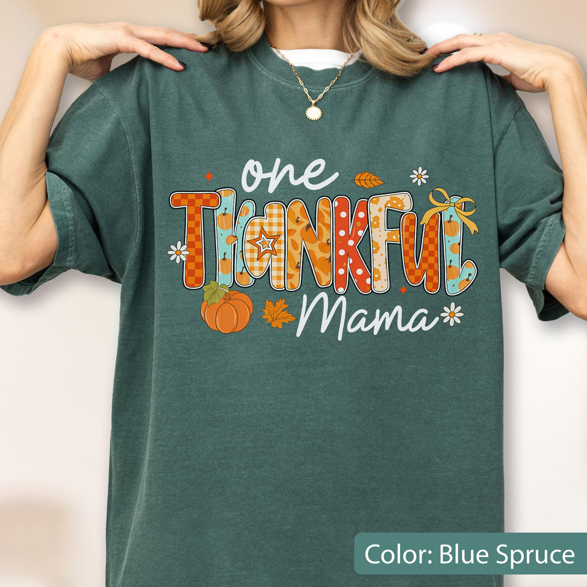May include: Blue spruce-colored t-shirt with the text "one THANKFUL Mama" in a colorful, fall-themed design. The design includes pumpkins, leaves, and floral accents. The shirt is a comfortable, casual style.