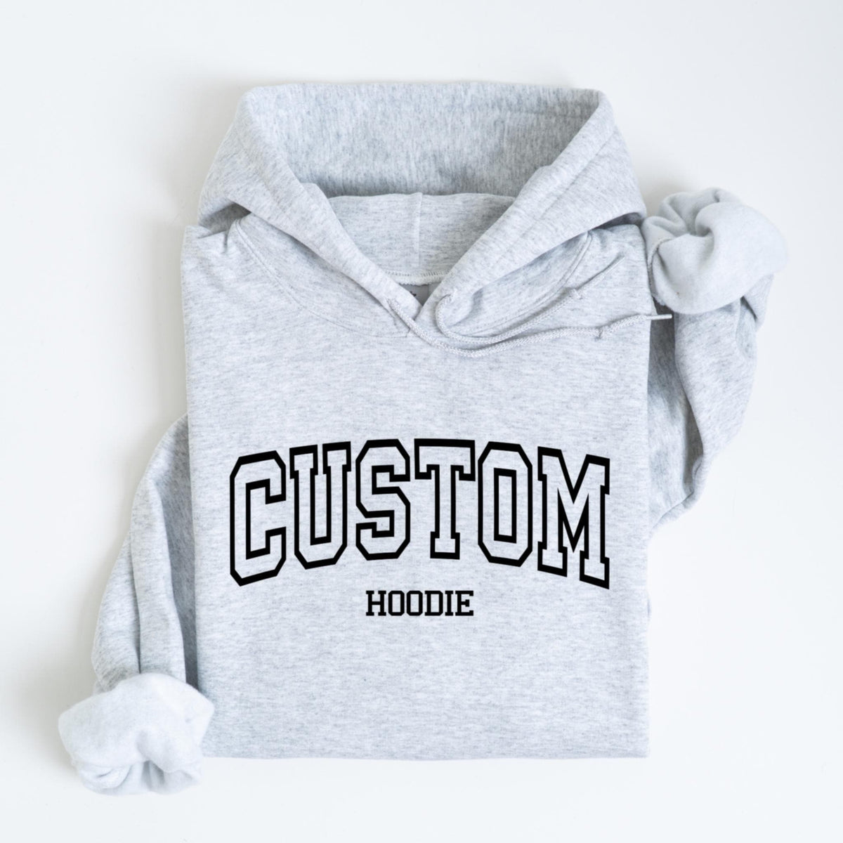 May include: A light gray hoodie with the word "CUSTOM" in a black, collegiate-style font across the chest. Below the word "CUSTOM" is the word "HOODIE" in a smaller, black font. The hoodie has a hood and long sleeves.