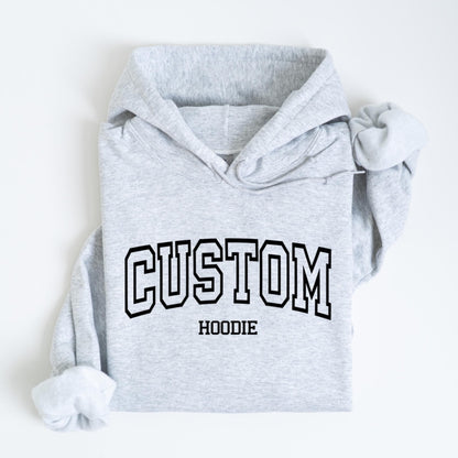 May include: A light gray hoodie with the word "CUSTOM" in a black, collegiate-style font across the chest. Below the word "CUSTOM" is the word "HOODIE" in a smaller, black font. The hoodie has a hood and long sleeves.