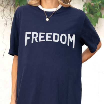 May include: Navy blue t-shirt with the word "FREEDOM" in large white capital letters. The shirt has a white collar and is worn with a gold necklace.