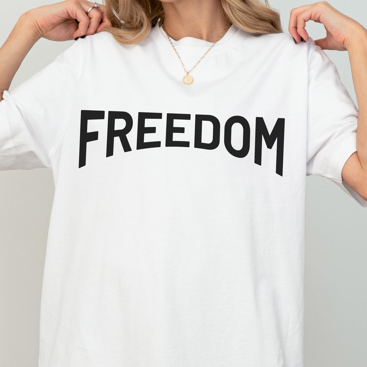 May include: White t-shirt with the word "FREEDOM" printed in large, black, bold letters across the front. The shirt has short sleeves and a crew neck. The overall style is casual and simple.