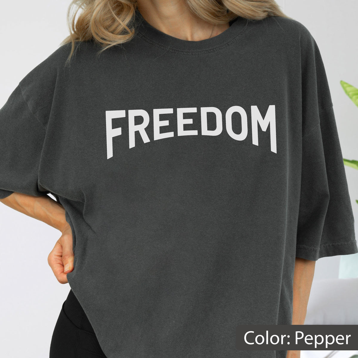 May include: A dark gray, oversized t-shirt with the word "FREEDOM" printed in large, white capital letters across the chest. The shirt is a solid color and has short sleeves. The color is described as "Pepper".