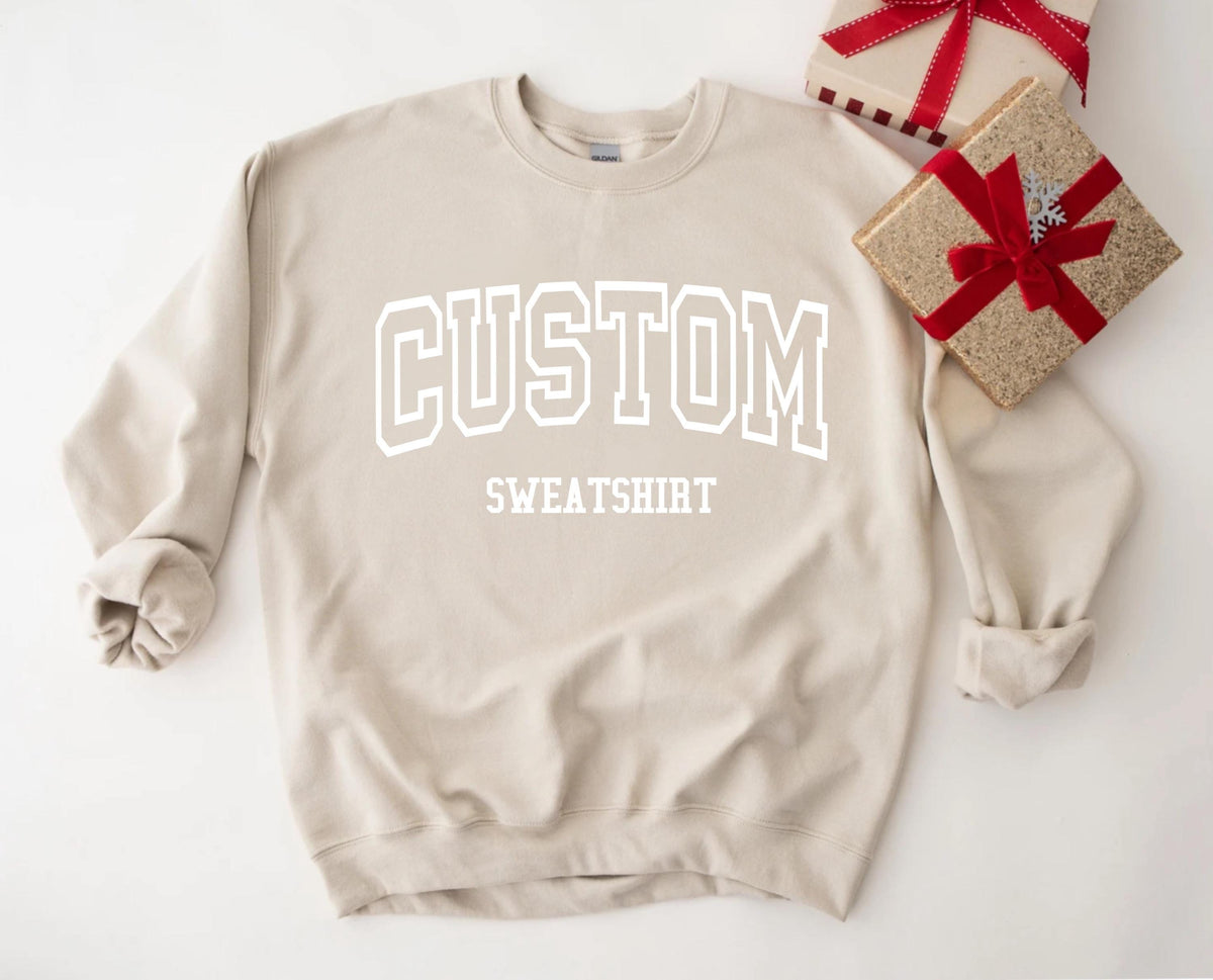 May include: A beige sweatshirt with the word "CUSTOM" in white, block letters. Below it, the word "SWEATSHIRT" is also in white. Two gift boxes with red ribbons are in the background.