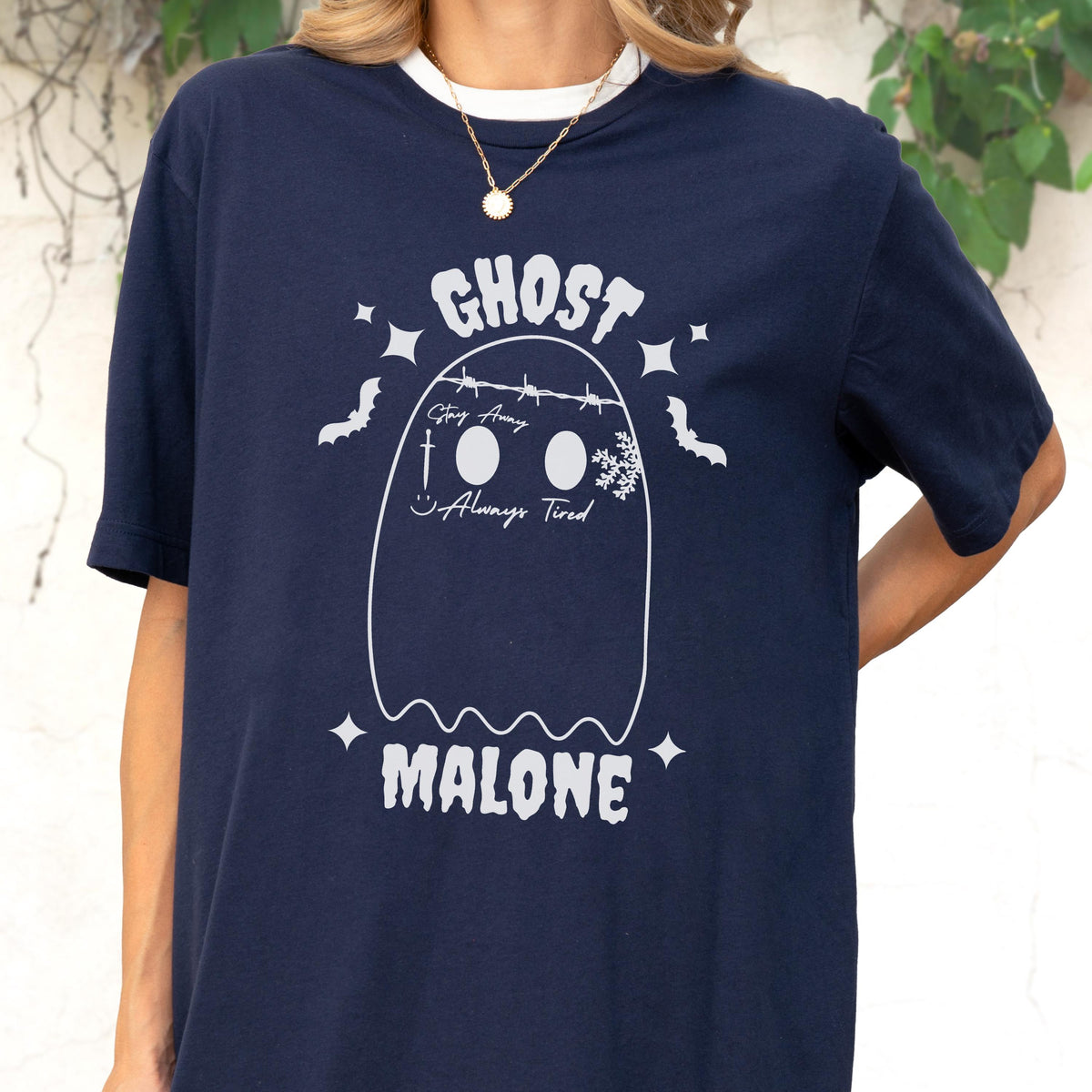 May include: A navy blue short-sleeve t-shirt featuring a white graphic of a ghost with barbed wire across the top, a sword, a snowflake, and the text "GHOST MALONE", "Stay Away", and "Always Tired" printed on the front with small bat icons.