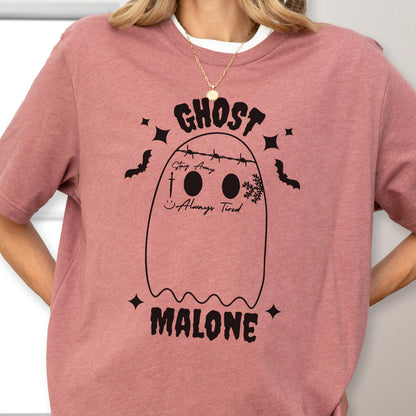 May include: A dusty rose t-shirt featuring a black graphic of a ghost with barbed wire across its head. The ghost has the text Stay Away, a sword, a smiley face, and Always Tired printed on it. The word GHOST is above and MALONE is below.