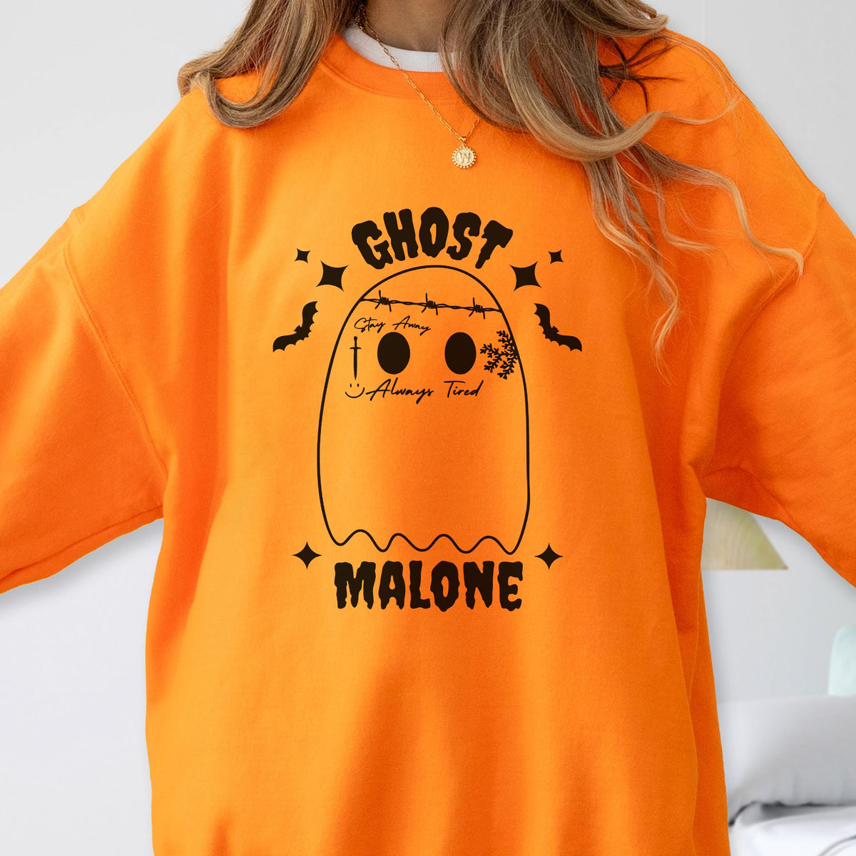 May include: Bright orange sweatshirt featuring a ghost design with the text "GHOST MALONE". The ghost has two black eyes, a smiling mouth, and the words "Stay Away" and "Always Tired". Black bats and stars surround the ghost.