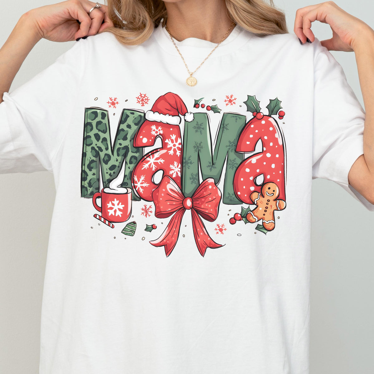 May include: White t-shirt with a festive "MAMA" graphic. The letters feature a mix of patterns: leopard print, snowflakes, and red polka dots. A red bow, gingerbread man, and Santa hat complete the holiday design.