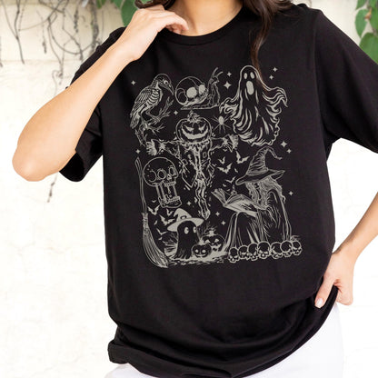 May include: Black t-shirt featuring a detailed, light gray graphic of Halloween-themed illustrations. The design includes a witch, skulls, a ghost, a pumpkin, bats, and a broom. The shirt is made of a soft material.