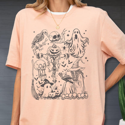 May include: A light peach-colored t-shirt featuring a black and white Halloween-themed graphic. The design includes a witch, ghosts, pumpkins, bats, and other spooky elements. The shirt has a crew neck and short sleeves.