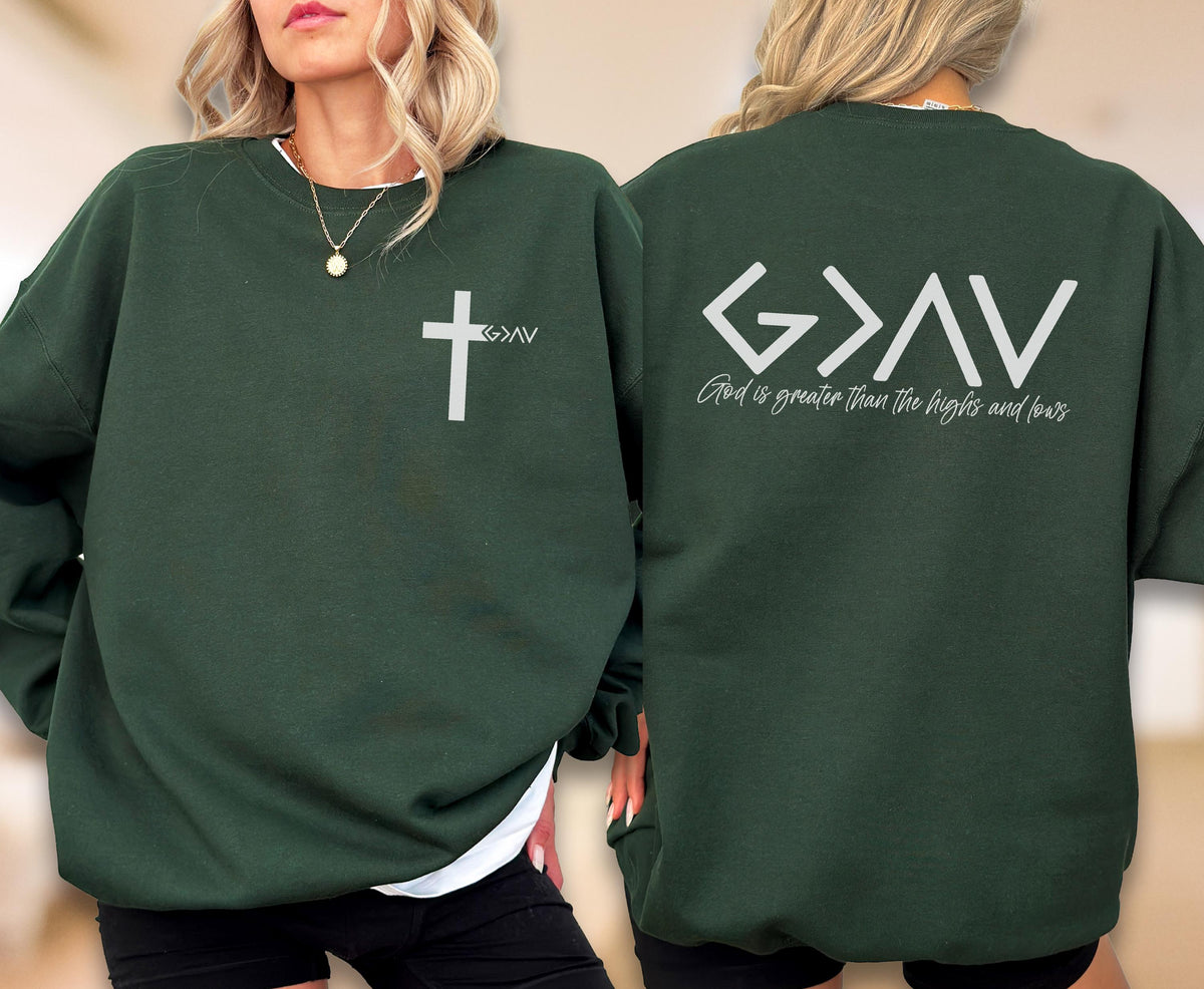 May include: A dark forest green crewneck sweatshirt featuring a white cross graphic with the text G>AV on the front left chest and the text G>AV with the phrase God is greater than the highs and lows printed in white on the back of the garment.