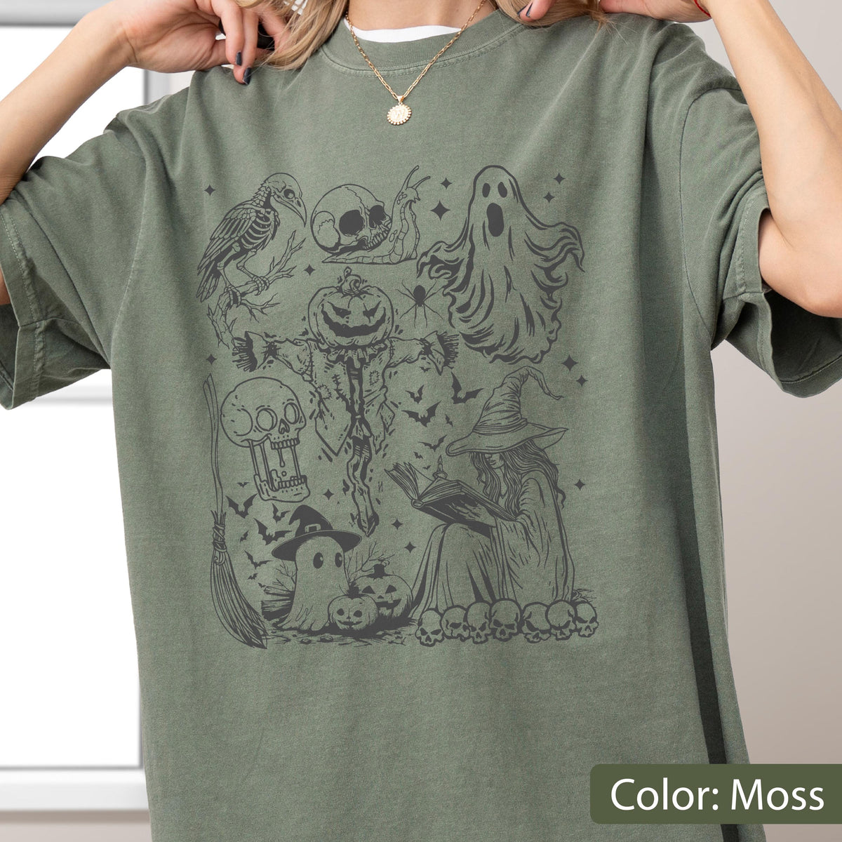 May include: Moss green t-shirt featuring a Halloween-themed graphic. The design includes a crow, skull, ghost, scarecrow, witch, bats, and pumpkins. The text "Color: Moss" is at the bottom right.