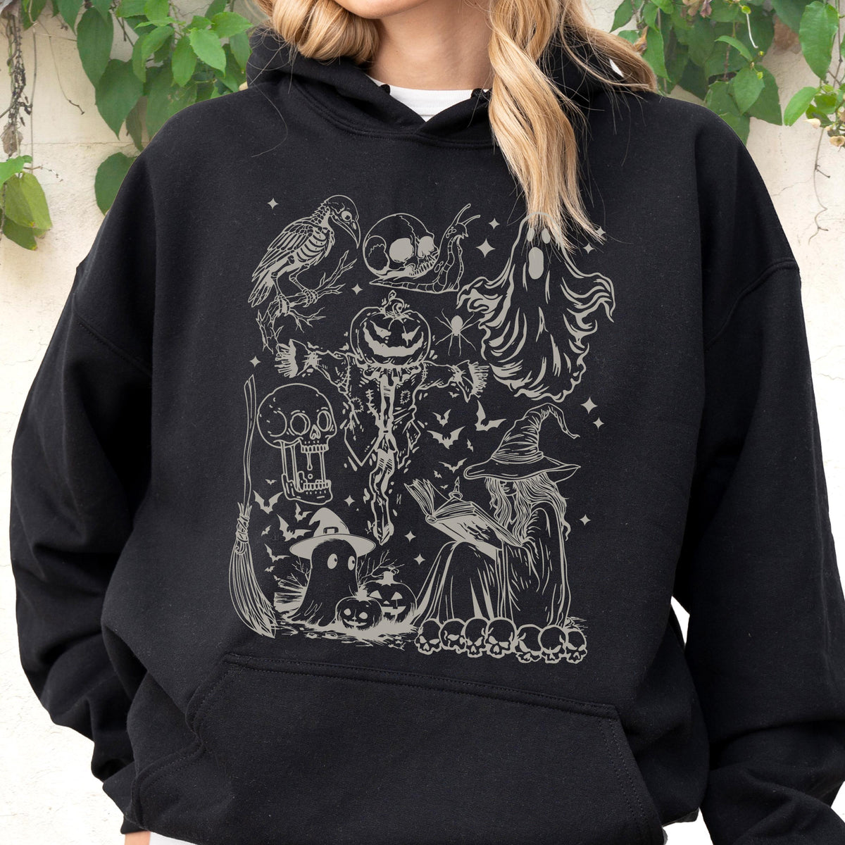May include: Black hooded sweatshirt featuring a detailed, grayscale Halloween-themed graphic. The design includes a witch, pumpkins, ghosts, bats, and skulls. The overall aesthetic is spooky and suitable for the Halloween season.