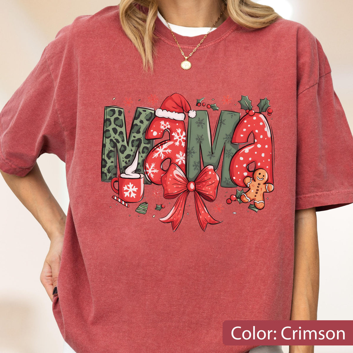 May include: Crimson-colored t-shirt with the word "MAMA" in a festive Christmas design. The letters feature leopard print, snowflakes, a Santa hat, and a gingerbread man. A red bow and holly complete the holiday theme.