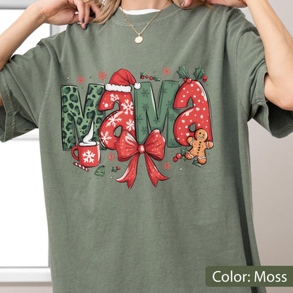 May include: Moss green t-shirt with a festive "MAMA" design. The letters are decorated with Christmas elements: a Santa hat, snowflakes, a red bow, and a gingerbread man. The "M" has a leopard print pattern. A red mug with a snowflake is also featured.