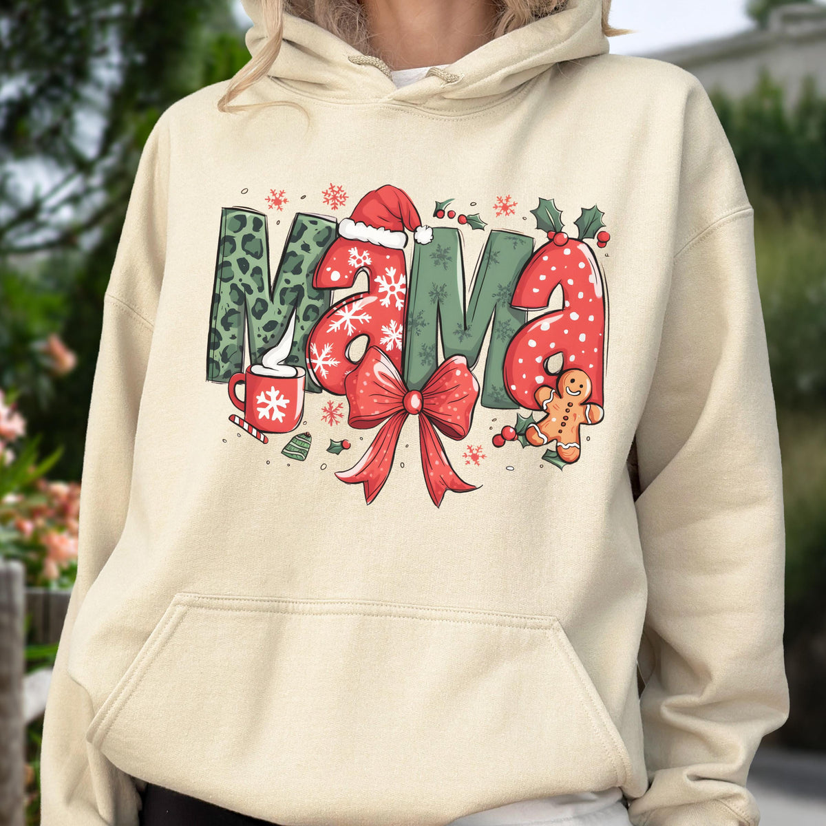 May include: Beige hoodie with a festive "MAMA" graphic. The letters are decorated with Christmas elements: leopard print, snowflakes, a Santa hat, a red bow, holly, and a gingerbread man. A mug with a snowflake design is also featured.