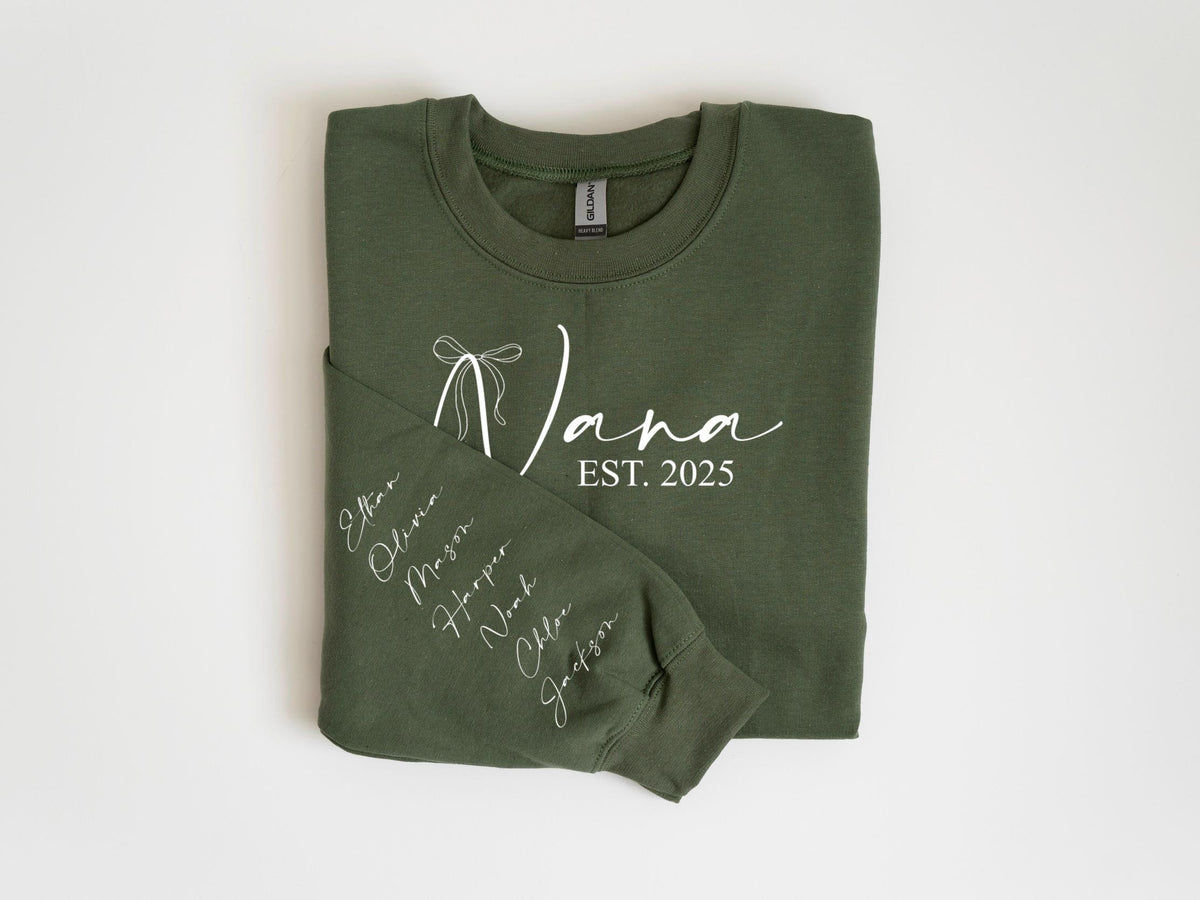 May include: Olive green sweatshirt with the word "Nana" in white script, a bow graphic, and "EST. 2025". The left sleeve displays names in white script. A cozy, personalized gift.