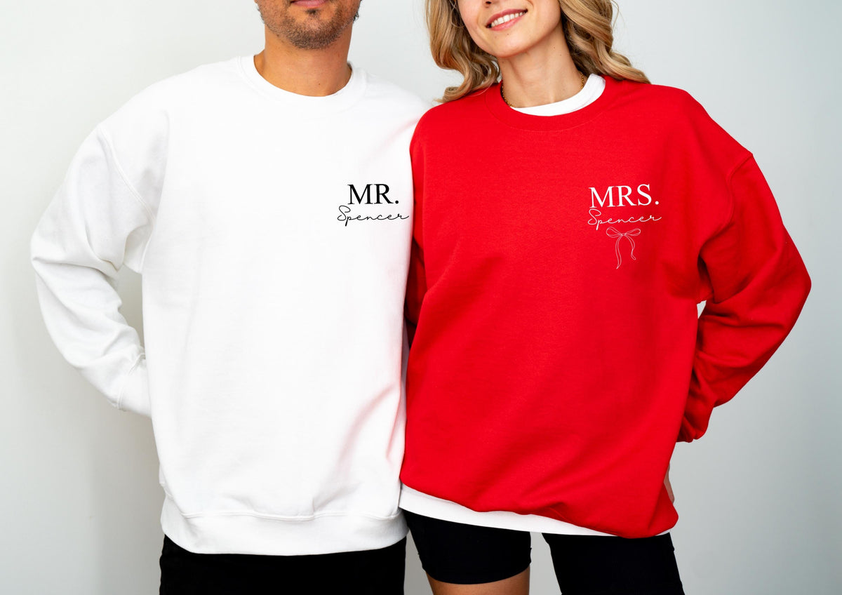 May include: A white and a red sweatshirt. The white sweatshirt has "MR. Spencer" printed on the front. The red sweatshirt has "MRS. Spencer" printed on the front with a bow graphic. Both sweatshirts are long-sleeved.