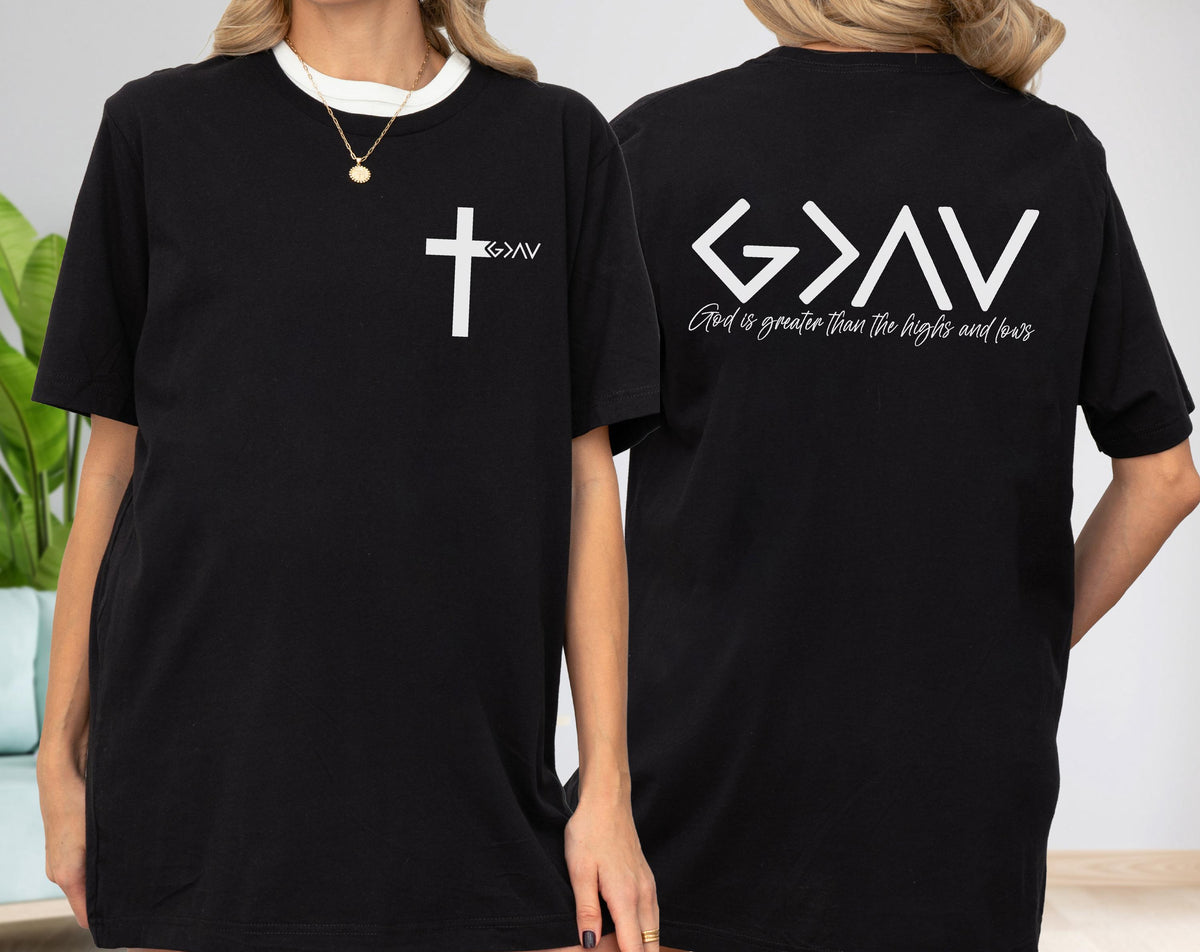 May include: Black t-shirt with white text and a cross graphic on the front. The back of the shirt features the text "God is greater than the highs and lows". The shirt has a crew neck and short sleeves.