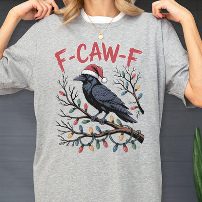 May include: A heather gray t-shirt featuring a black raven wearing a red and white Santa hat perched on a bare tree branch. The branch is decorated with colorful Christmas lights. Above the raven, the text F-CAW-F is printed in red letters.
