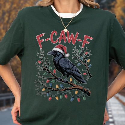 May include: A dark green t-shirt featuring a graphic of a black crow wearing a red and white Santa hat, perched on a branch wrapped in colorful Christmas lights. The text F-CAW-F is printed in red above the crow. A gold chain necklace is worn.