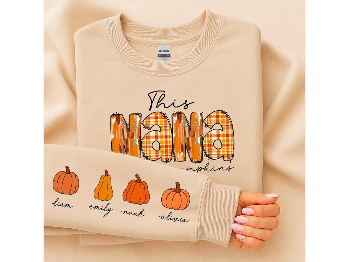 May include: Beige sweatshirt with the text "This NANA" in a plaid design. The sleeve features orange pumpkin illustrations and names: Liam, Emily, Noah, and Olivia. A fall-themed garment.