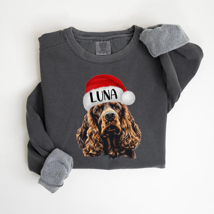 May include: Dark gray sweatshirt featuring a Cocker Spaniel wearing a Santa hat with the name "LUNA" printed on it. The sleeves have a gray, fuzzy lining. The sweatshirt is a comfortable, casual style.