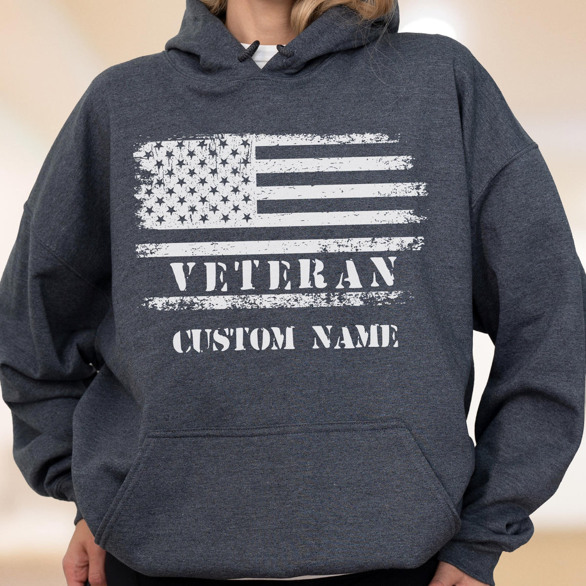 May include: Dark gray hooded sweatshirt featuring a distressed white American flag design. The text "VETERAN" and "CUSTOM NAME" are printed below the flag. The sweatshirt has a drawstring hood and a front pocket.