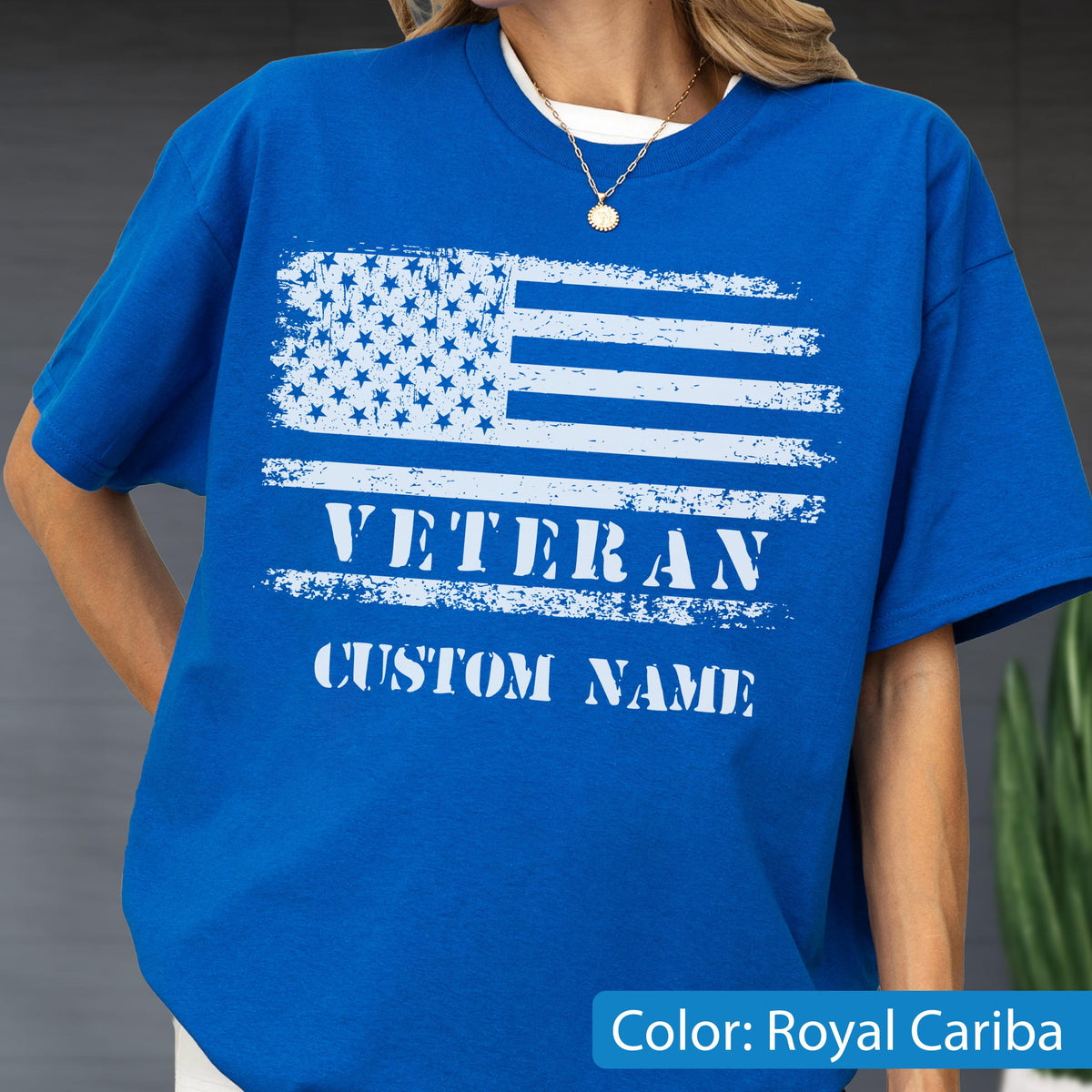 May include: A royal blue short-sleeve t-shirt featuring a distressed white graphic of the American flag. Below the flag, the word VETERAN is printed in a bold, distressed white font, followed by the text CUSTOM NAME in a matching white style.