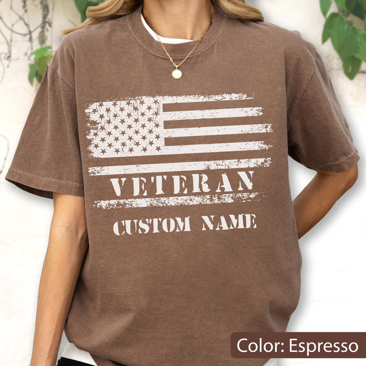 May include: An espresso-colored short-sleeve t-shirt featuring a distressed white graphic of the American flag. Below the flag, the word VETERAN is printed in a bold, distressed white font, followed by the text CUSTOM NAME in the same style.