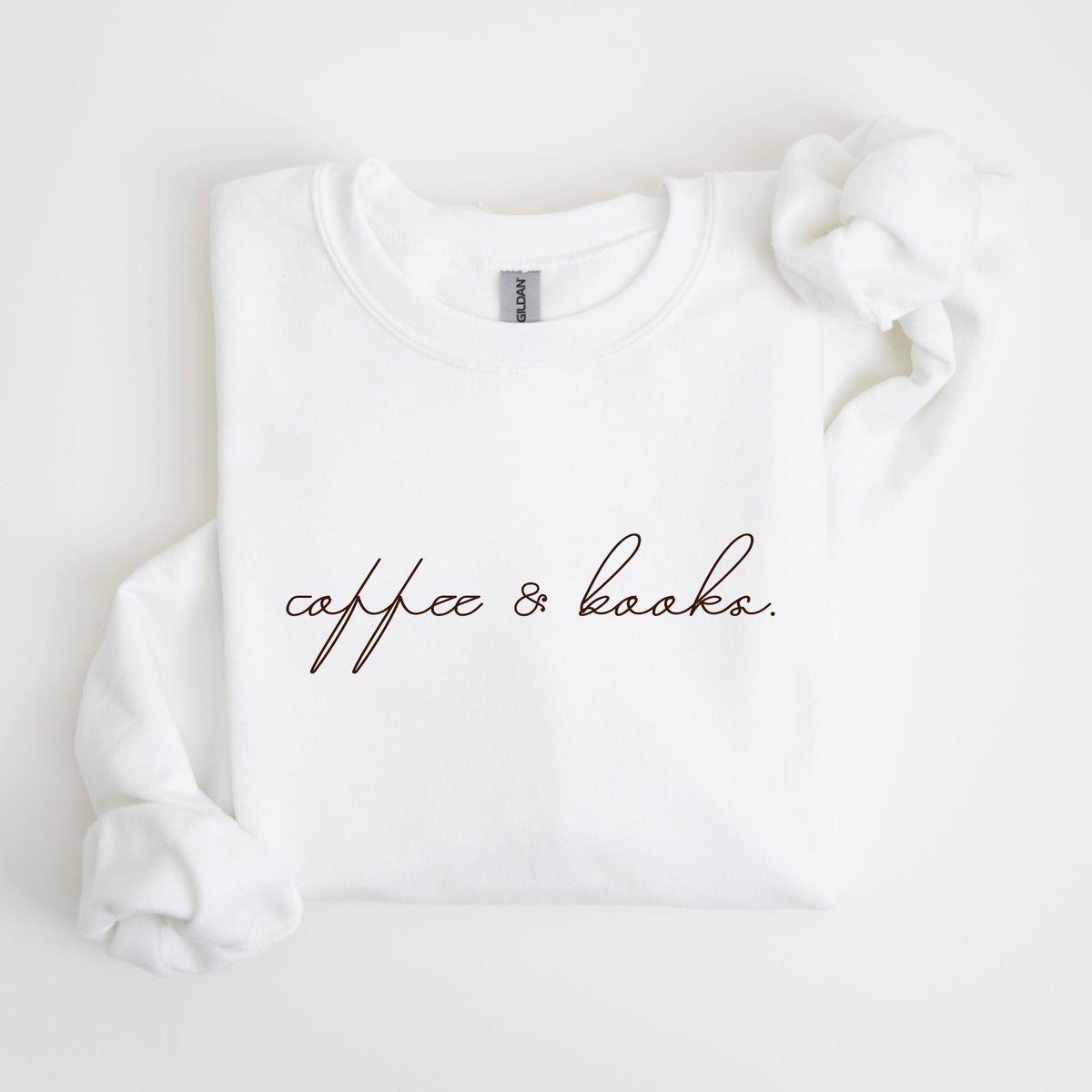 May include: White crew neck sweatshirt with the words "coffee & books" in a brown script font. The sweatshirt is made of a soft material and has a relaxed fit. The sleeves are folded over.