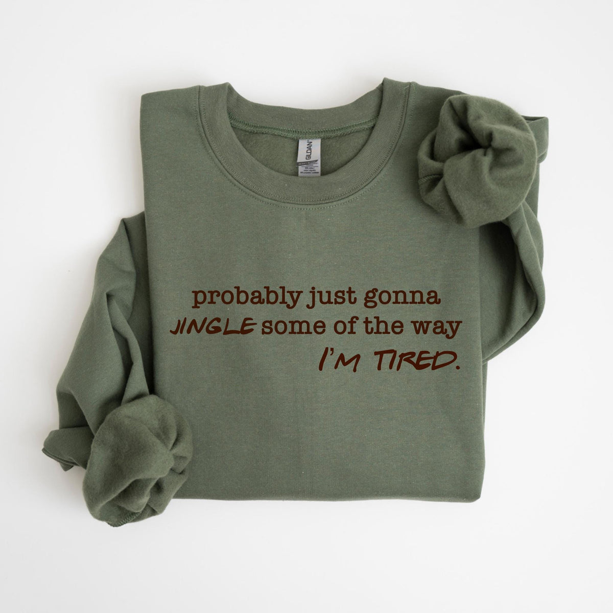 May include: Olive green sweatshirt with the text "probably just gonna JINGLE some of the way I'M TIRED" in a dark brown color. The sweatshirt is folded with one sleeve rolled up.