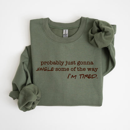 May include: Olive green sweatshirt with the text "probably just gonna JINGLE some of the way I'M TIRED" in a dark brown color. The sweatshirt is folded with one sleeve rolled up.